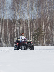 A winter forest. A woman with ginger hair riding snowmobile