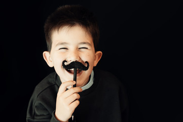 Happy kid posing with a fake moustache on black background