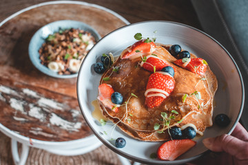 Bright plate with a healthy summer Breakfast American pancakes with berries and a power bowl made of natural yogurt cereal and banana on a wooden background
