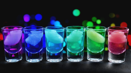 Variation of hard alcoholic shots with ice served on bar counter. Blur neon background