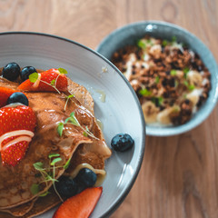 Bright plate with a healthy summer Breakfast American pancakes with berries and a power bowl made of natural yogurt cereal and banana on a wooden background