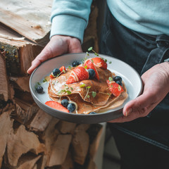 Healthy summer breakfast: delicious american pancakes with fresh strawberries and blueberries and honey carried on a plate by a waitress