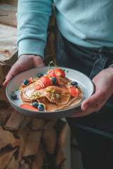 Healthy summer breakfast: delicious american pancakes with fresh strawberries and blueberries and honey carried on a plate by a waitress