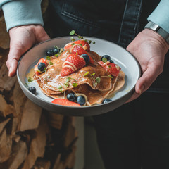 Healthy summer breakfast: delicious american pancakes with fresh strawberries and blueberries and honey carried on a plate by a waitress