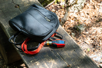Small women's backpack and electronic cigarette on wooden bench in a forest