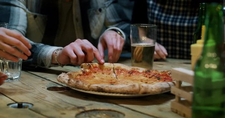 Slow motion close up of friends eating italian pizza and drinking beer at restaurant or pub. Shot in 8k. Concept of college friends, holidays, food and drink