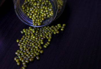 various grains are laying on a dark wooden table through bottles 