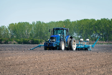 a large blue tractor prepares the land for planting