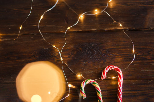  Christmas candies and lights on wooden background. Christmas concept, mint striped lollipops and a garland of lights, as a background for the Christmas party