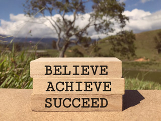 Motivational and inspirational words - Believe, Achieve, Succeed written on rectangular wood blocks.