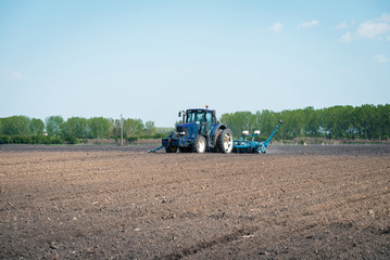 a large blue tractor prepares the land for planting