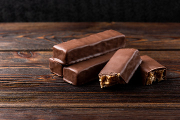 Chocolate bar with caramel and peanut on dark wooden background. 
