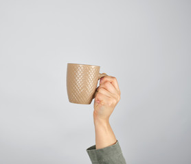 female hand holding a brown ceramic mug with a drink