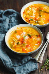 Spring vegetable soup with chicken broth for two person on wooden table. Rustic style, close-up view.