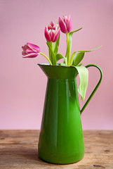 Pink tuplis flowers in green vase on the pink background