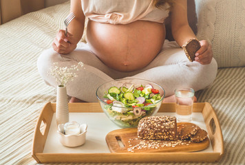 Pregnancy and healthy organic nutrition. Pregnant woman enjoying fresh vegetable salad in bed, free space. Concept of expectation and health.