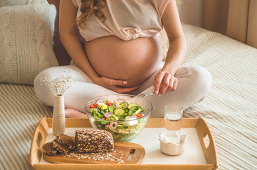 Pregnancy and healthy organic nutrition. Pregnant woman enjoying fresh vegetable salad in bed, free...