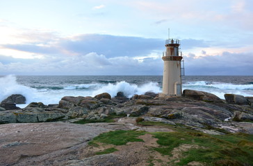 Old lighthouse and waves breaking against the rocks with sunset light. Muxia, Spain.