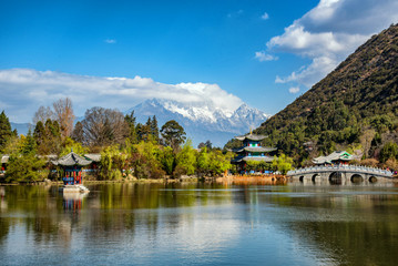 Fototapeta premium Niesamowity widok na Śnieżną Górę Jadeitowego Smoka i sadzawkę Czarnego Smoka, Lijiang, prowincja Junnan, Chiny. Most Suocui nad stawem i pawilon obejmujący księżyc w Jade Spring Park.