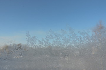 A close-up of beautiful ice flowers on a window, blue sky in the background © E-lona