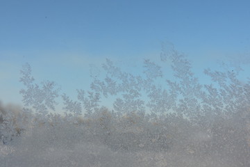 A close-up of beautiful ice flowers on a window, blue sky in the background © E-lona