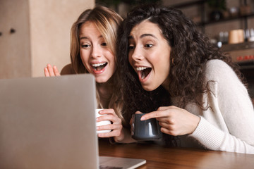 Two cheerful young girls friends sitting at the cafe table