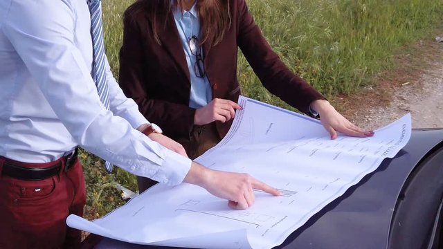 Coppia di Ingegneri sta osservando il progetto su carta, poggiato sulla macchina. Attivit&agrave; industriale nel cantiere sulla costa di un pontile in costruzione.