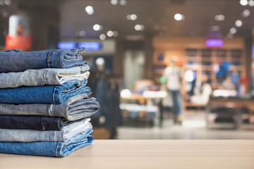 Blue denim jeans stack on wood table top with abstract blur clothing store in modern shopping mall defocused bokeh light background