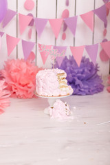 Photo zone with paper garlands, balloons, paper balls, pom poms, confetti and cream cake. Birthday cake. Smash cake. One year. Pink, white, violet, rose colors