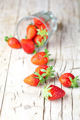 Organic red strawberries in glass on rustic wooden background.