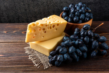 Blue grapes and cheese on dark wooden background.