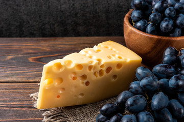 Blue grapes and cheese on dark wooden background.