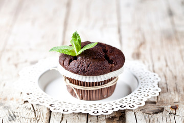 Fresh dark chocolate muffin with mint leaves on white plate