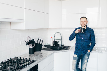 Young man smiling and holding coffee at home in the kitchen