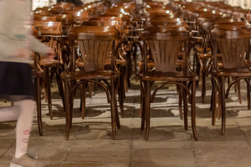 Fototapeta na wymiar Front view dramatic shoot of arrays of wooden chairs in old building hall while a girl running through