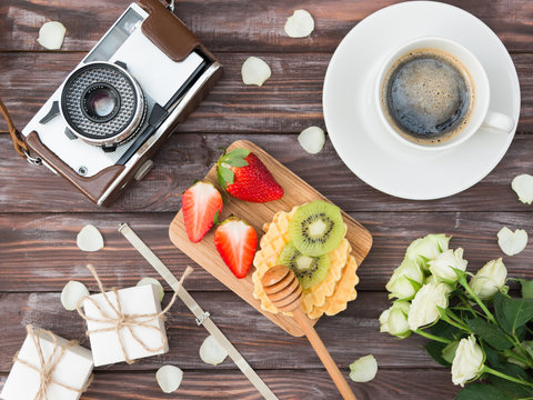 Spring holiday flat ley: roses, gift boxes with jewelry, bracelet with charms, camera,coffee, waffles, strawberries and kiwi. Congratulate your beloved on holiday. March 8. Mothers Day. Hugge. Lagom.