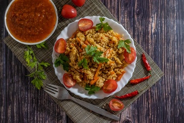 Pilaf and cherry tomatoes in a plate on a dark background, adzhika. Central Asian cuisine. Horizontal orientation. Hot peppers