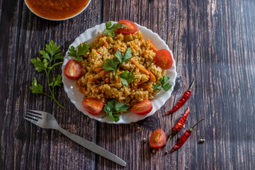 Pilaf and cherry tomatoes in plate on wooden background. Central Asian cuisine. Horizontal orientation. Hot peppers