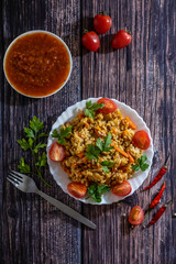 Pilaf and cherry tomatoes in a plate on a wooden background, adjika. Central Asian cuisine. Vertical orientation. Hot peppers