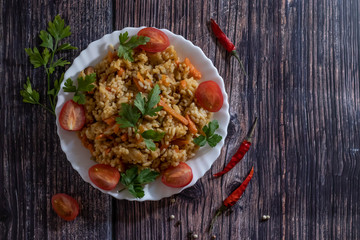 Pilaf and cherry tomatoes in plate on wooden background. Central Asian cuisine. Horizontal orientation. Hot peppers