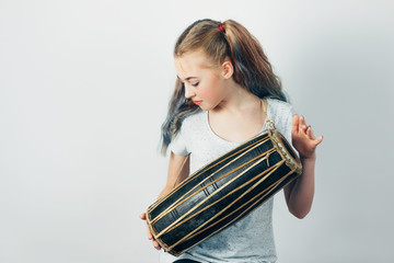 Beautiful teen girl playing ethnic hand drum mridangam on gray background. 