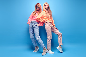 Fashion. Two hipster Girl in trendy colorful neon Outfit Fooling Around in Studio. Young Tomboy...