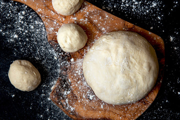 Dough for bread or pizza on a board. Black background