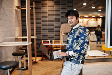 Young male indian freelancer sitting open laptop computer in fast food cafe, handsome asian man reading text message during work on net-book in comfortable coffee shop.