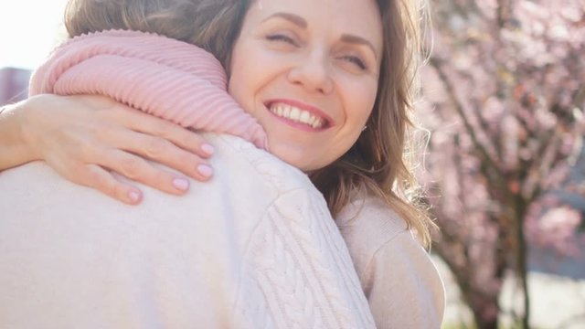 Middle-aged mother and her daughter hugging in blooming spring garden. Mothers day