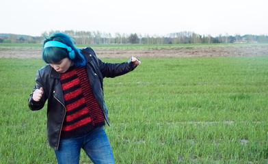 An interesting girl in blue hair, listens to music and dances in the field.