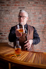 Man tasting whisky on a Bar in Front of a red stone wall