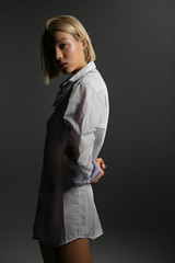 Fashion model. Young blond woman posing in studio wearing white shirt. Beautiful caucasian girl over gray background