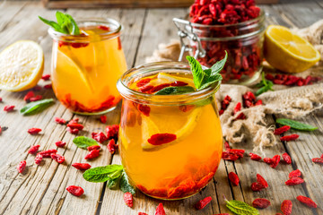 Homemade goji hot tea with mint and lemon slices, wooden rustic background copy space