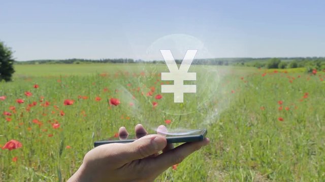 Hologram of Sign JPY on a smartphone. Person activates holographic image on the phone screen on the field with blooming poppies